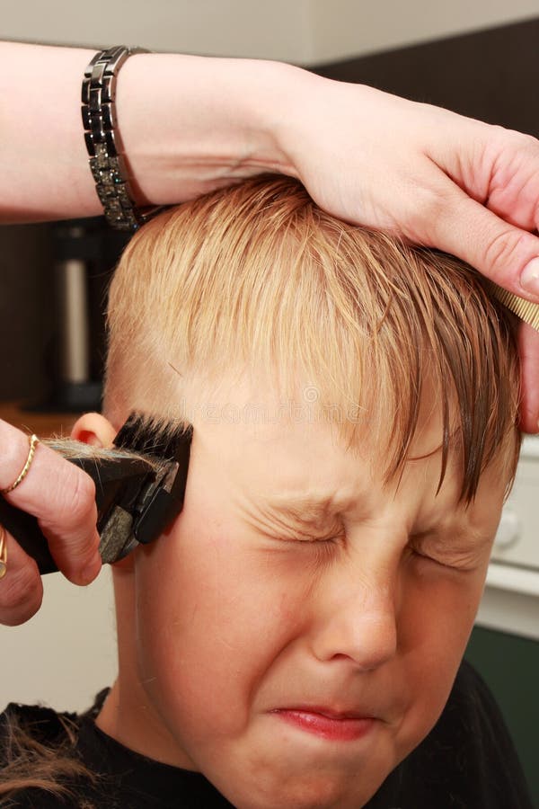 A professional hairdresser cutting a boys hair short, unhappy look on boys face. A professional hairdresser cutting a boys hair short, unhappy look on boys face