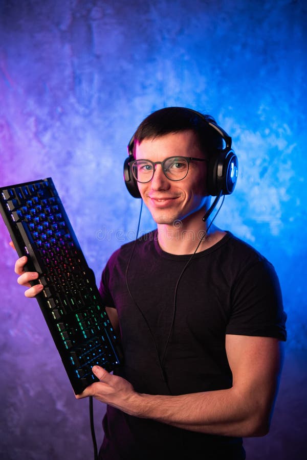 Профессиональный Gamer мальчика держа клавиатуру игры над красочным пинком и голубой неоновой свет стеной Концепция gamers игры стоковая фотография rf Профессиональный Gamer мальчика держа клавиатуру игры над красочным пинком и голубой неоновой свет стеной Концепция gamers игры стоковая фотография rf