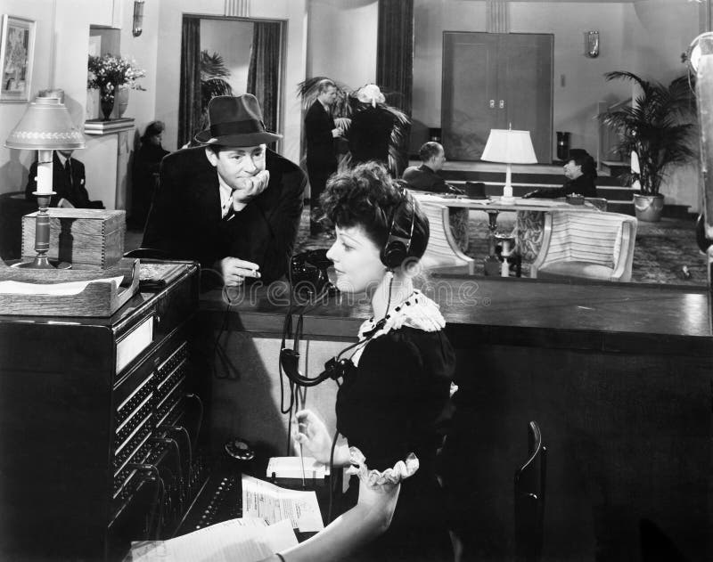 Profile of a woman working on the telephone switchboard with a man looking at her (All persons depicted are no longer living and no estate exists. Supplier grants that there will be no model release issues.). Profile of a woman working on the telephone switchboard with a man looking at her (All persons depicted are no longer living and no estate exists. Supplier grants that there will be no model release issues.)