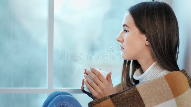 Профиль сиротливой прелестной женщины нося теплое усаживание свитера на windowsill и мысли