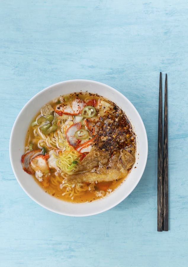 Spicy Thai style egg noodle soup with roasted pork in white bowl on blue wooden table background. Spicy Thai style egg noodle soup with roasted pork in white bowl on blue wooden table background