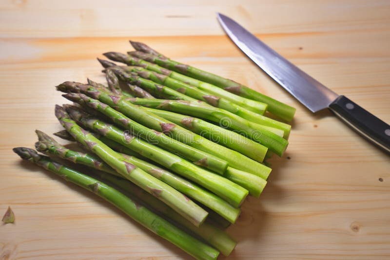 Пук зеленых свежих спаржи или spargel в немце на choping плите с кухонным ножом стоковые изображения rf Пук зеленых свежих спаржи или spargel в немце на choping плите с кухонным ножом стоковые изображения rf