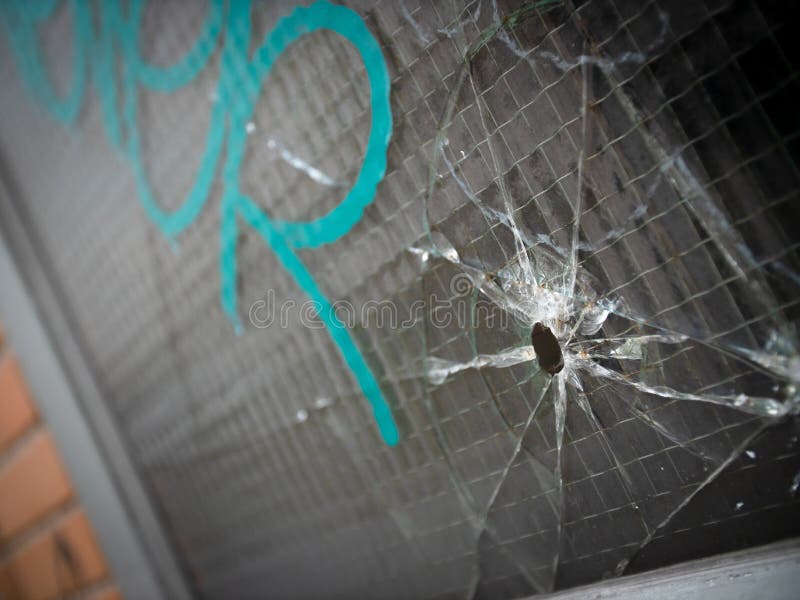 Bullet hole and cracks in a reinforced window with gang graffiti. Bullet hole and cracks in a reinforced window with gang graffiti