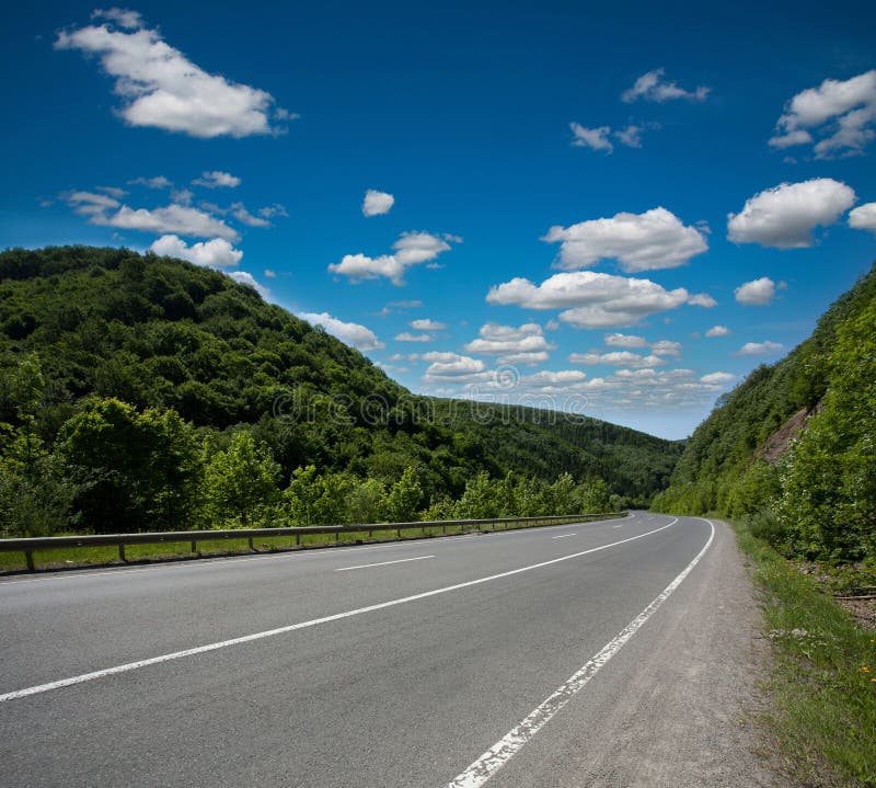 Empty asphalt road highway in the forested mountains, on the background a cloudy sky. Empty asphalt road highway in the forested mountains, on the background a cloudy sky