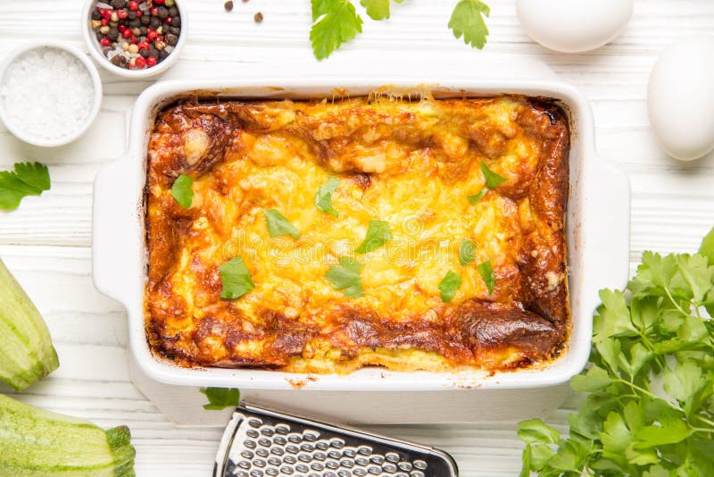 Пушистый омлет испеченный с цукини, завтраком детей здоровым, вкусным сотейником На белой деревянной предпосылке, в печь блюде стоковая фотография rf Пушистый омлет испеченный с цукини, завтраком детей здоровым, вкусным сотейником На белой деревянной предпосылке, в печь блюде стоковая фотография rf