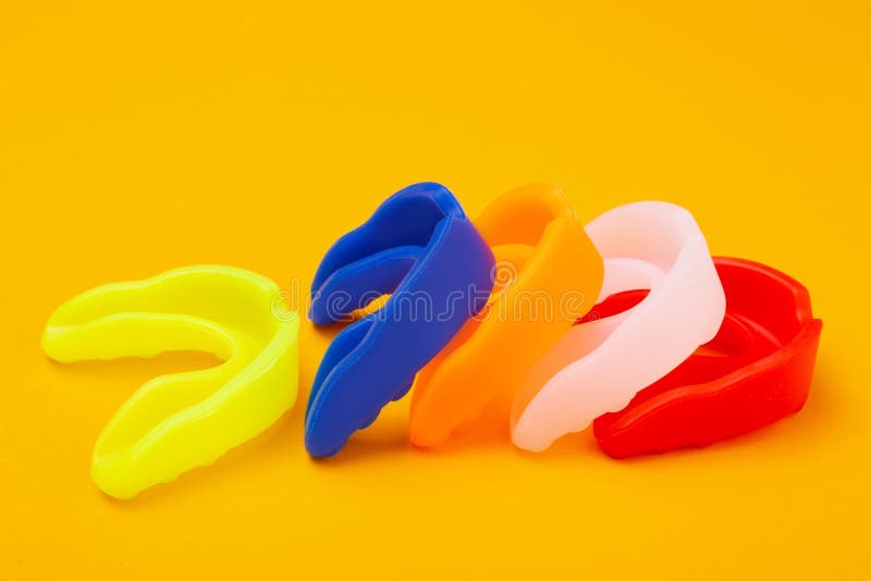 Five colored boxing mouth guards laid out in a row on a yellow background, concept, horizontal layout. Five colored boxing mouth guards laid out in a row on a yellow background, concept, horizontal layout