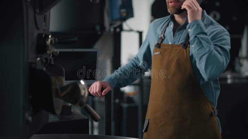 Работник кавказской фабрики по производству жареного кофе, работающий рядом с обжаривающей машиной с какао-бобами, перемешивающими видеоматериал