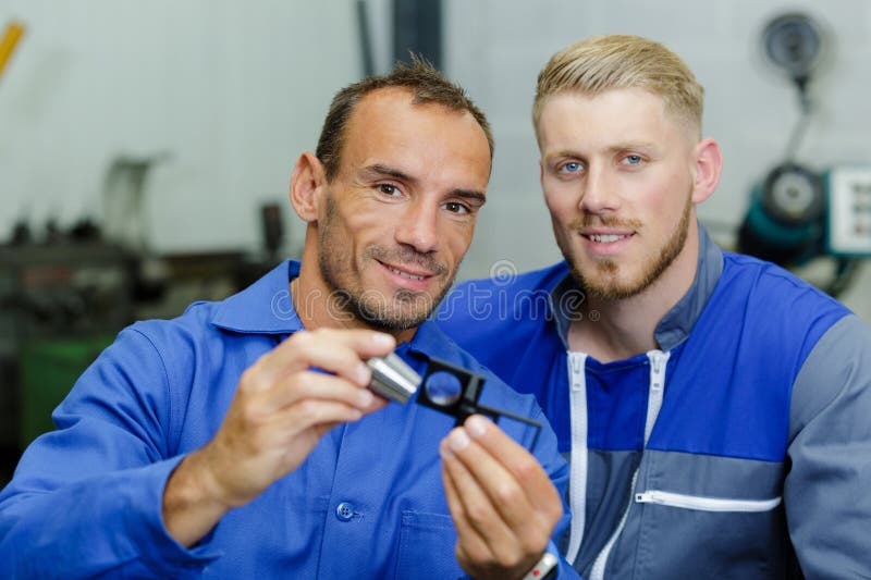 2 workers looking at a metalic piece indoors. 2 workers looking at a metalic piece indoors