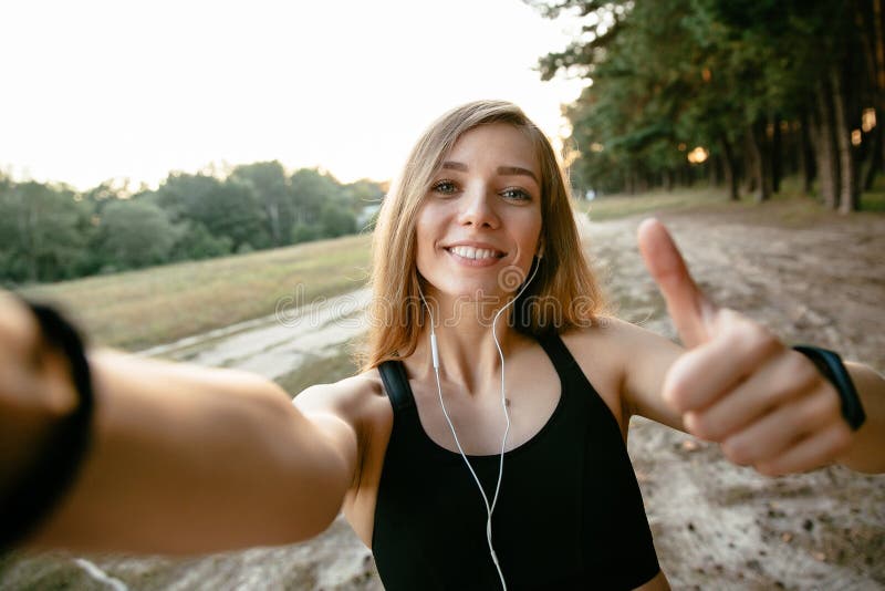 Радостная девушка показывая большой палец руки вверх пока принимающ selfie, outdoors стоковая фотография