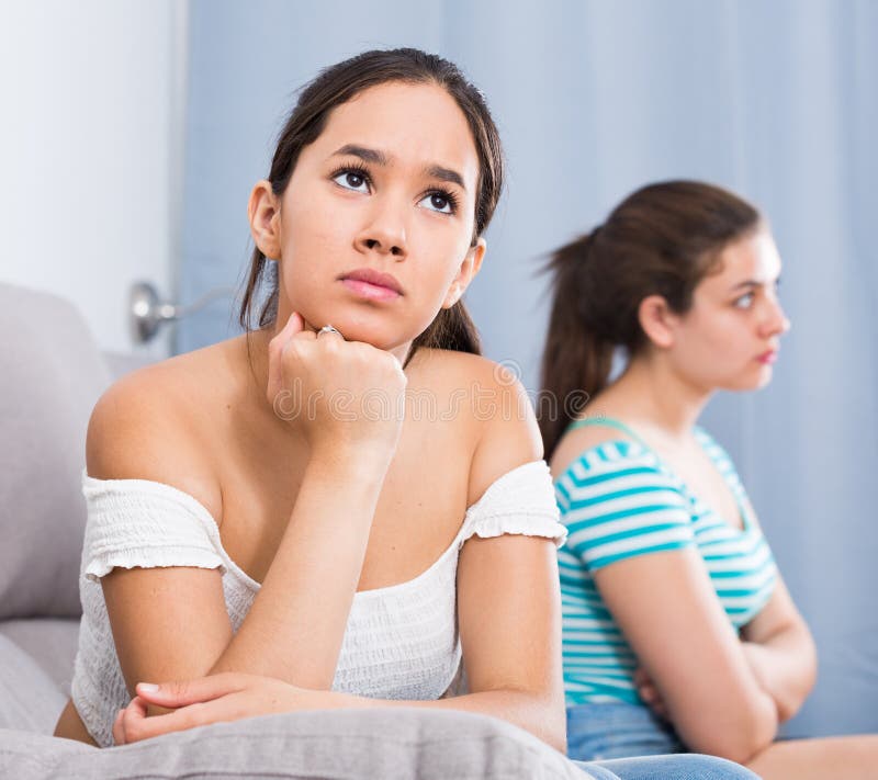 Two angry quarreled teenage girls sitting apart on couch at home. Two angry quarreled teenage girls sitting apart on couch at home