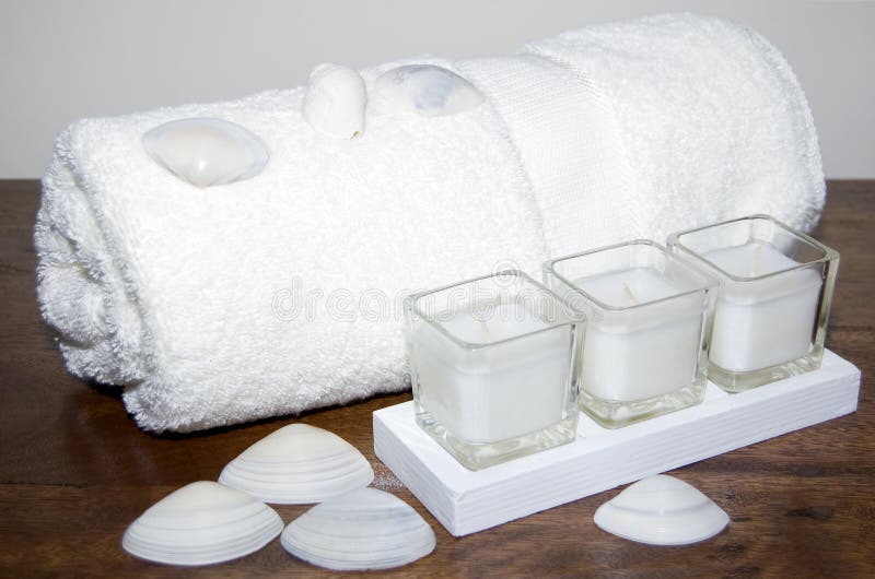 White towel with white seashells and candles on contrasting timber shelf. White towel with white seashells and candles on contrasting timber shelf