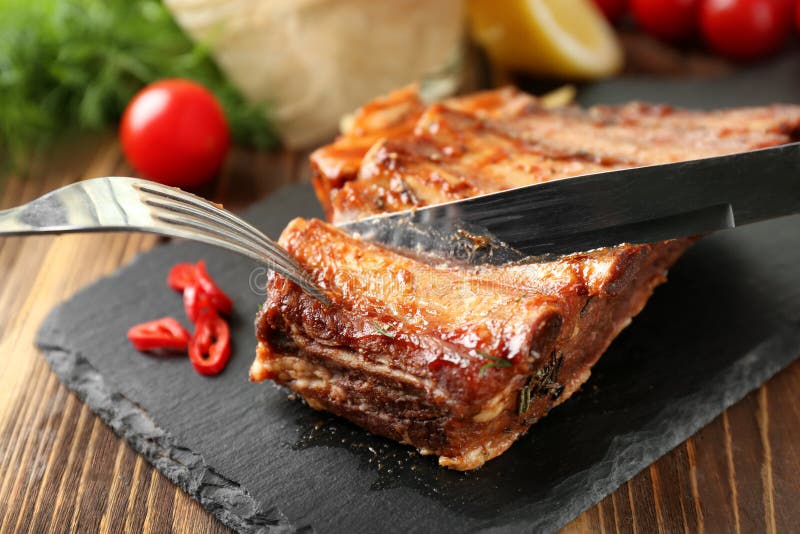 Резать очень вкусных зажаренных нервюр на плите шифера стоковое изображение rf Резать очень вкусных зажаренных нервюр на плите шифера стоковое изображение rf