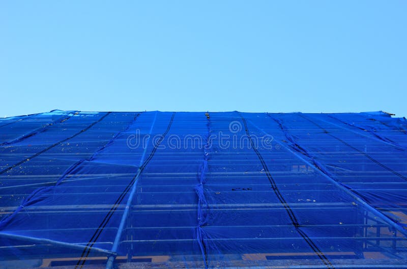 Repair of the facade of the house. The scaffolding is covered with a blue transparent net made of plastic fabric. protects settlers as well as pedestrians so that pieces of concrete bricks and objects. Repair of the facade of the house. The scaffolding is covered with a blue transparent net made of plastic fabric. protects settlers as well as pedestrians so that pieces of concrete bricks and objects