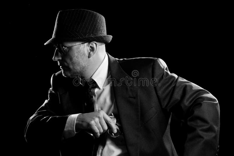 Photo of man shot with studio lighting, holding a handgun, with Fedora Hat, Dark Suit and Sun Glasses. Photo of man shot with studio lighting, holding a handgun, with Fedora Hat, Dark Suit and Sun Glasses.