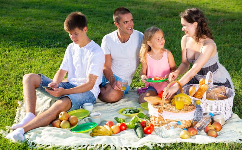 Родители с двумя подростками наслаждаются вкусной едой на пикнике стоковые изображения Родители с двумя подростками наслаждаются вкусной едой на пикнике стоковые изображения
