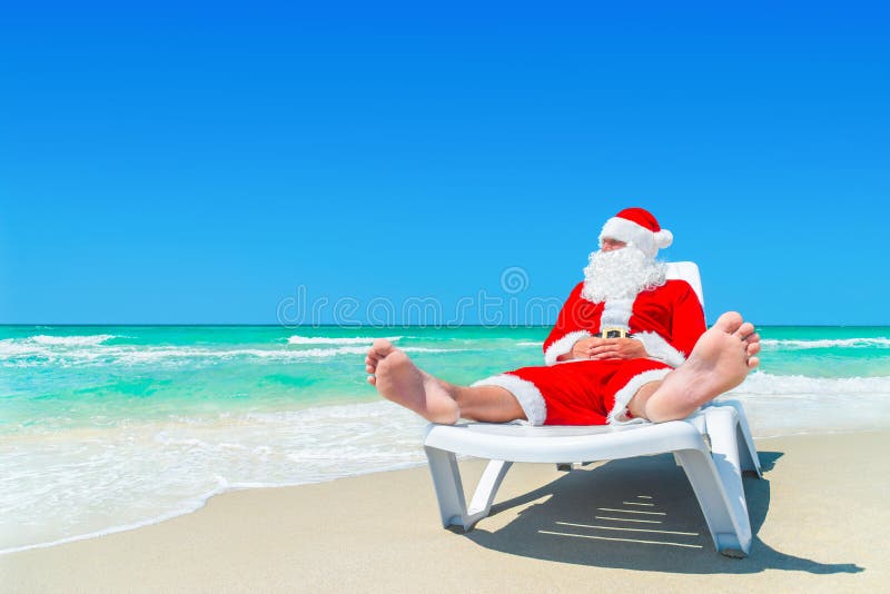 Рождество Санта Клаус ослабляет на sunlounger на пляже океана тропическом стоковые фотографии rf