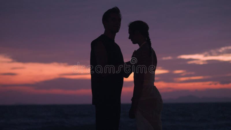 романтическая пара муж и жена делят прекрасный момент на вечернем пляже на закате. муж нежно целует жену