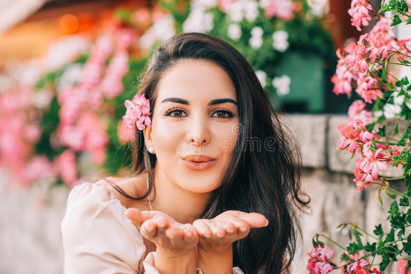 Close up portrait of beautiful young woman with long shiny hair, posing outdoor in pink flowers, sending a kiss. Close up portrait of beautiful young woman with long shiny hair, posing outdoor in pink flowers, sending a kiss