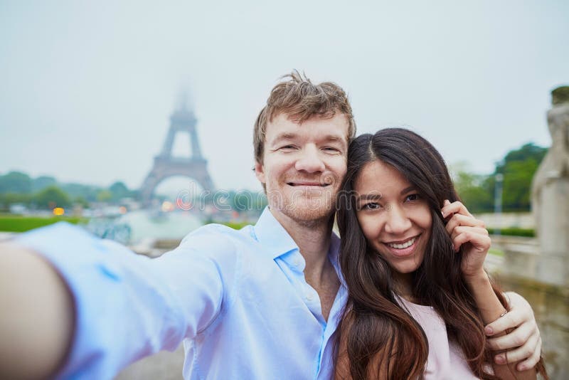 Романтичные пары в влюбленности принимая selfie около Эйфелевой башни в Париже на пасмурный и туманный дождливый день стоковые изображения rf Романтичные пары в влюбленности принимая selfie около Эйфелевой башни в Париже на пасмурный и туманный дождливый день стоковые изображения rf