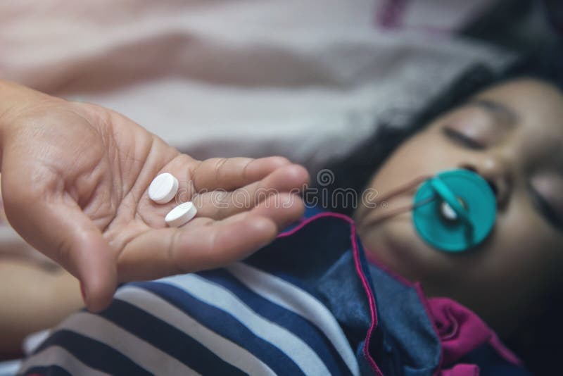 Рука держа таблетки медицины над азиатским ребенк с pacifier в ее рте стоковое изображение Рука держа таблетки медицины над азиатским ребенк с pacifier в ее рте стоковое изображение