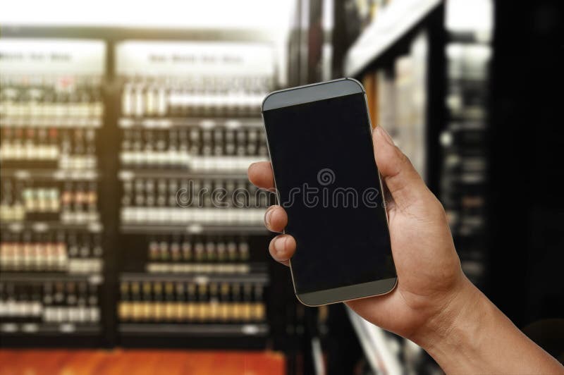 Рука держа smartphone на магазине супермаркета вина стоковые изображения rf Рука держа smartphone на магазине супермаркета вина стоковые изображения rf