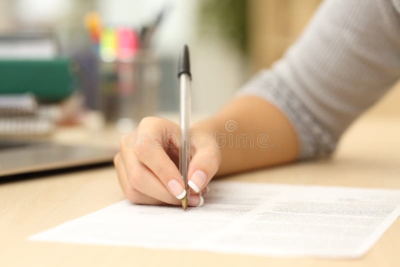 Close up of a woman hand writing or signing in a document on a desk at home or office. Close up of a woman hand writing or signing in a document on a desk at home or office