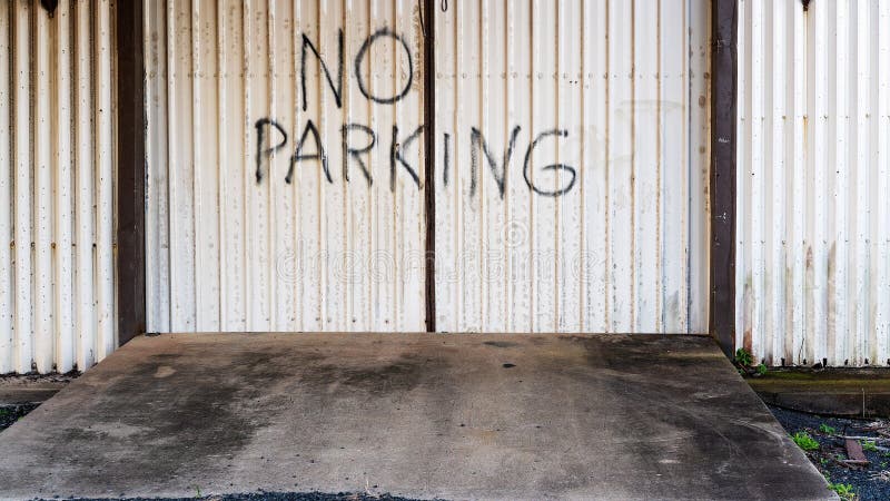 Hand written warning no parking sign on old metal doors in front of dirty concrete entry to abandoned building. Hand written warning no parking sign on old metal doors in front of dirty concrete entry to abandoned building