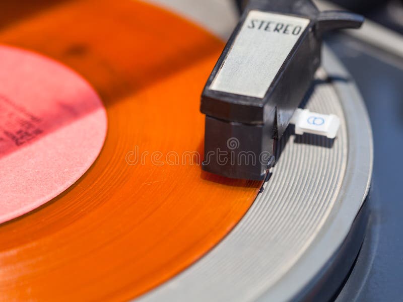 Tonearm of record-player on orange vinyl disc close up. Tonearm of record-player on orange vinyl disc close up