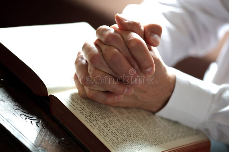 High key hands clasped in prayer on an open bible in church. High key hands clasped in prayer on an open bible in church