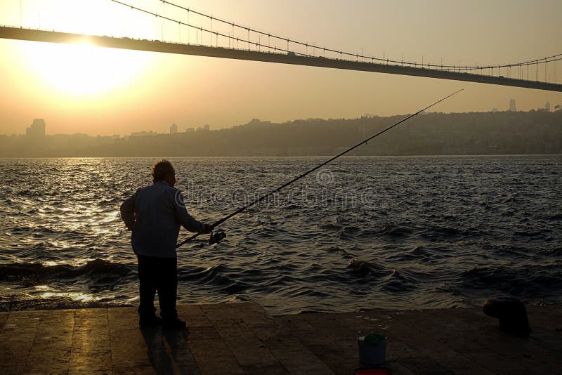 Рыбная ловля человека на побережье перед мостом bosphorus стоковая фотография rf Рыбная ловля человека на побережье перед мостом bosphorus стоковая фотография rf