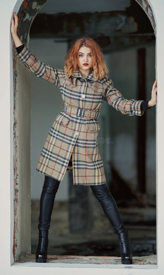 Рыжеволосая маленькая девочка в коротком checkered пальто и черных призонных брюках в высоких пятках представляет в получившемся стоковые изображения rf Рыжеволосая маленькая девочка в коротком checkered пальто и черных призонных брюках в высоких пятках представляет в получившемся стоковые изображения rf