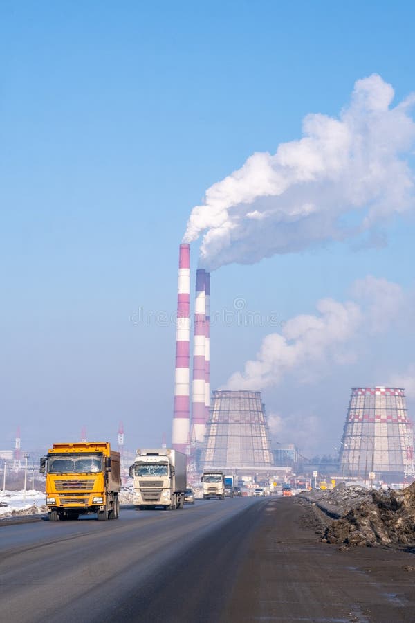 Naberezhnye Chelny, Russia, March 2, 2024. A convoy of vehicles drives down the asphalt road past the factory, smoke billowing from the chimneys into the sky. Naberezhnye Chelny, Russia, March 2, 2024. A convoy of vehicles drives down the asphalt road past the factory, smoke billowing from the chimneys into the sky.