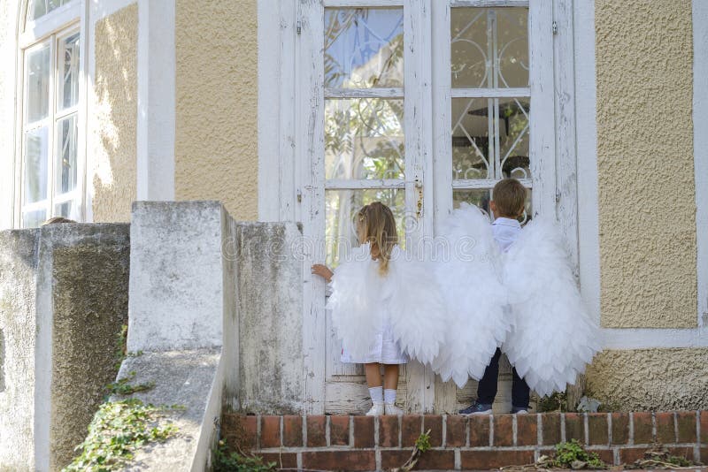 С niños vestidos como ángeles parados frente a una puerta cerrada fotos de archivo libres de regalías
