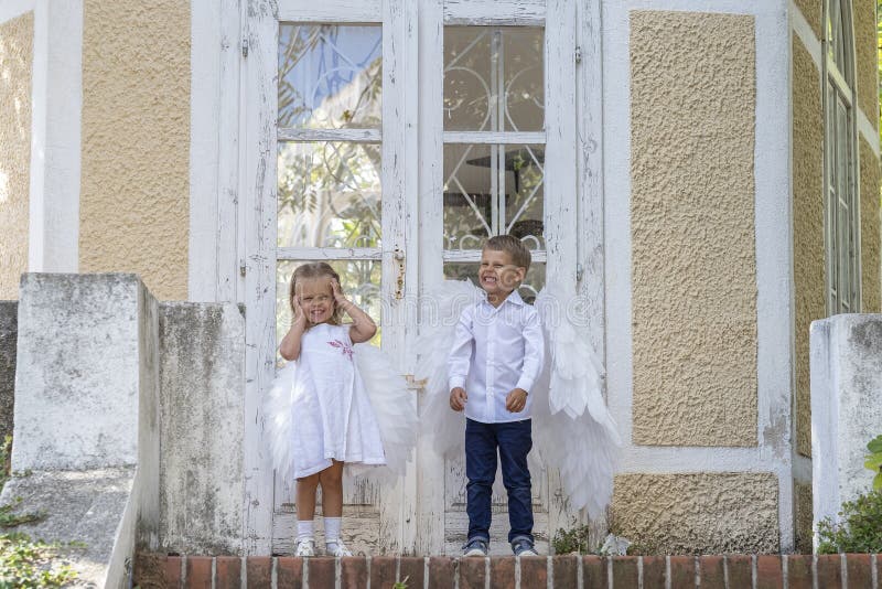 С niños vestidos como ángeles parados frente a una puerta cerrada imágenes de archivo libres de regalías
