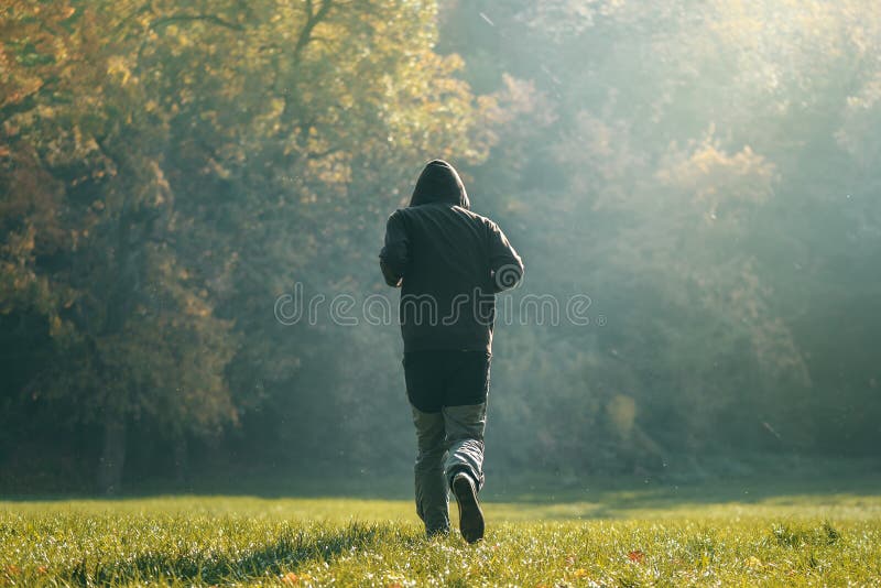 С капюшоном человек jogging в парке в предыдущем утре осени стоковое фото rf