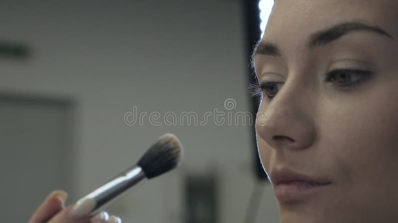 с специальной макияжной щёткой профессиональный художник делает макияж для красивой женской модели акции видеоматериалы
