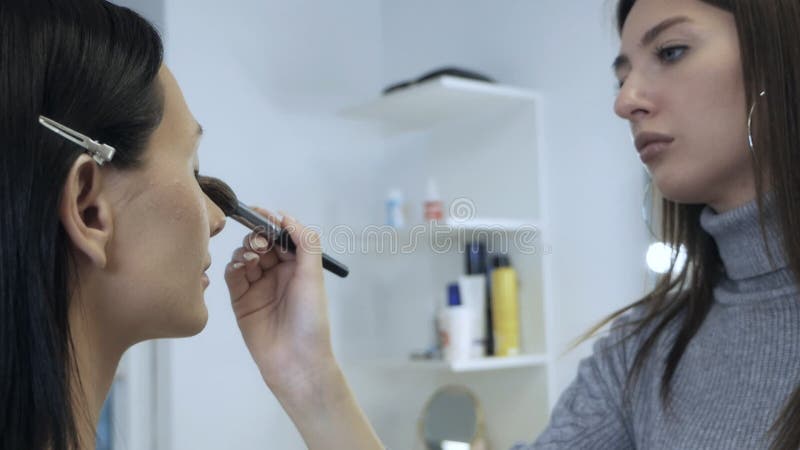 с специальной макияжной щёткой профессиональный художник делает макияж для красивой женской модели сток-видео