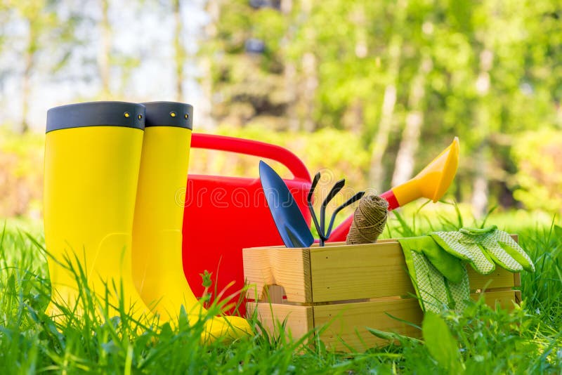 Garden tools, watering can and gardener`s boots close-up in the backyard of the house. Garden tools, watering can and gardener`s boots close-up in the backyard of the house