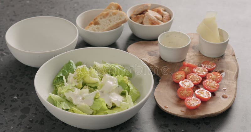 Салат и соусом romaine смеси руки человека для того, чтобы сделать салат цезаря в белом керамическом шаре на конкретном countertop стоковые фотографии rf