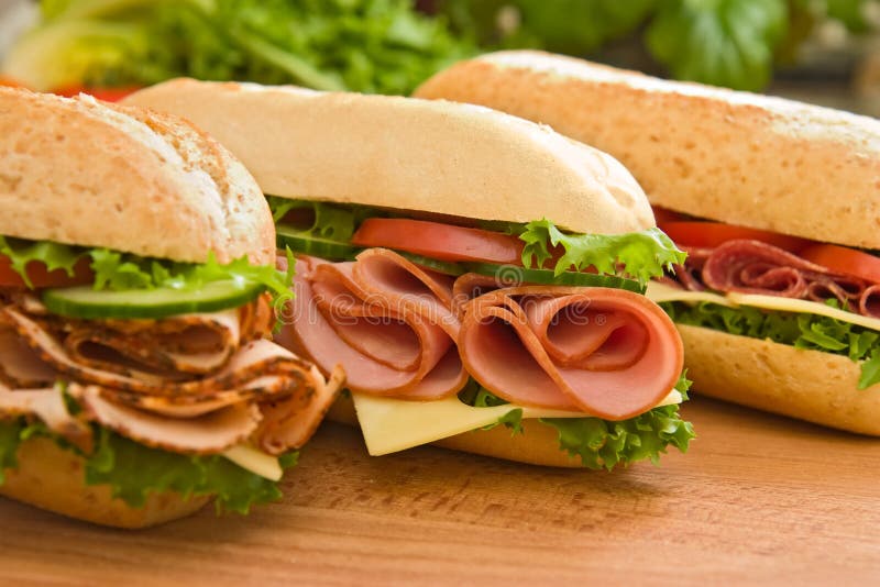 Three fresh sub sandwiches - turkey breast, ham & swiss and salami on a cutting board. Focus on the ham sandwich. Three fresh sub sandwiches - turkey breast, ham & swiss and salami on a cutting board. Focus on the ham sandwich