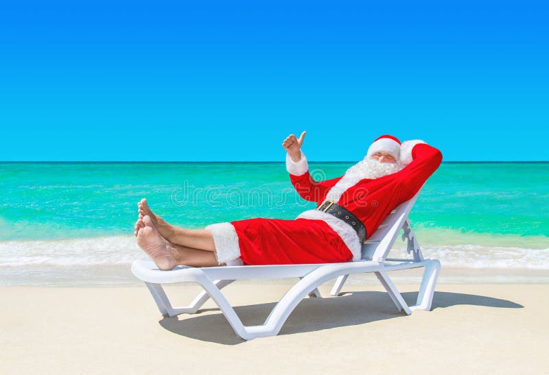 Санта Клаус thumbs вверх по показывать на sunlounger на тропическом пляже стоковые фотографии rf