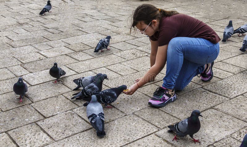 Sarajevo, Bosnia - May 2, 2022 - Young girl feeds the pigeons in a park. Sarajevo, Bosnia - May 2, 2022 - Young girl feeds the pigeons in a park.