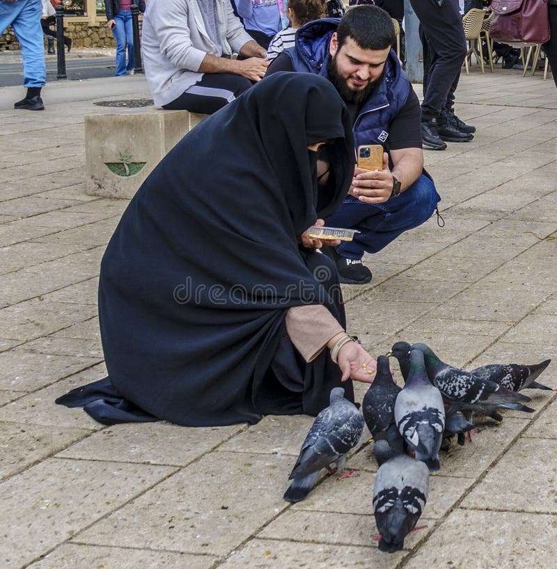 Sarajevo, Bosnia - May 2, 2022 - Young girl in burque feeds the pigeons in a park. Sarajevo, Bosnia - May 2, 2022 - Young girl in burque feeds the pigeons in a park.