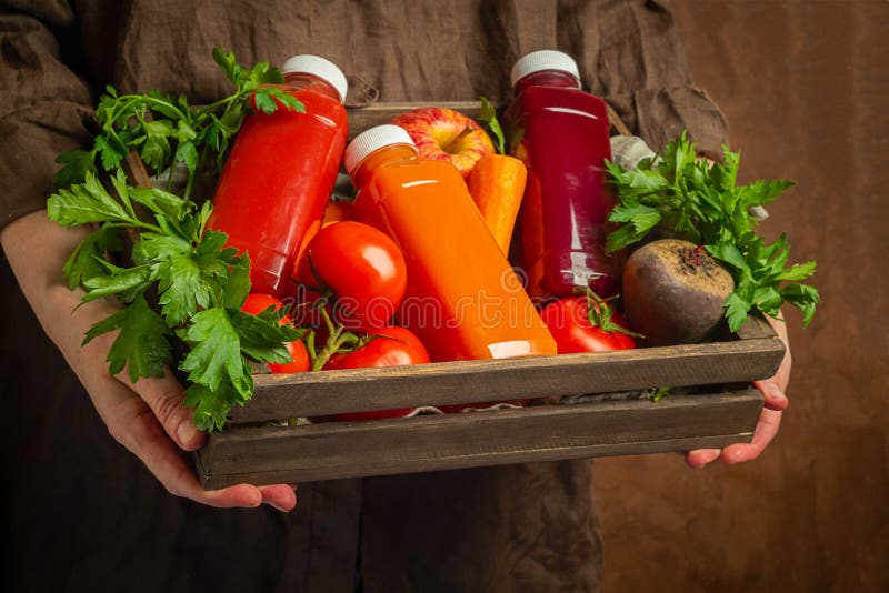 Свежие smoothies сока от различных томатов свеклы яблока моркови овощей в бутылках в деревянной коробке в женских руках стоковое фото Свежие smoothies сока от различных томатов свеклы яблока моркови овощей в бутылках в деревянной коробке в женских руках стоковое фото