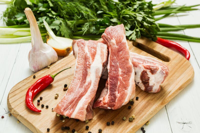 Свежие сырцовые нервюры свинины со слоями сала с овощами и перцем на разделочной доске стоковое фото rf Свежие сырцовые нервюры свинины со слоями сала с овощами и перцем на разделочной доске стоковое фото rf