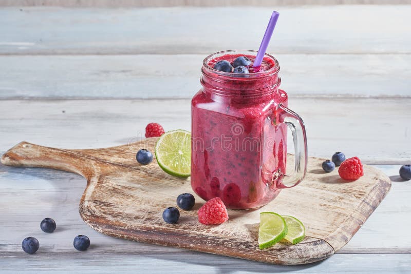 Свежий smoothie в стеклянном опарнике со зрелыми полениками, голубиками и известкой на деревенской разделочной доске стоковая фотография Свежий smoothie в стеклянном опарнике со зрелыми полениками, голубиками и известкой на деревенской разделочной доске стоковая фотография