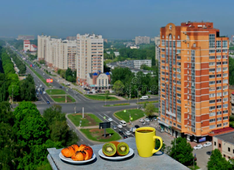 Светлый завтрак с панорамным видом города: румяная плюшка с маковыми семененами, несколько свежими кивиами и кружкой кофе стоковые изображения Светлый завтрак с панорамным видом города: румяная плюшка с маковыми семененами, несколько свежими кивиами и кружкой кофе стоковые изображения