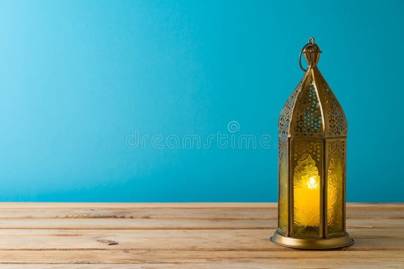 Lightened lantern on wooden table over blue background. Ramadan Kareem holiday celebration concept. Lightened lantern on wooden table over blue background. Ramadan Kareem holiday celebration concept