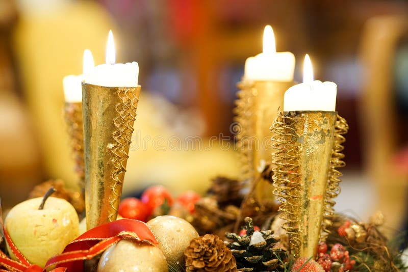 Four Christmas candles burning brightly in gold candlestick holders with an apple, fir cone and other decorations below. Four Christmas candles burning brightly in gold candlestick holders with an apple, fir cone and other decorations below.