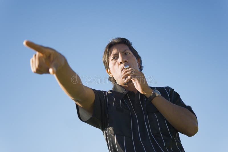 Low angle view of soccer referee whistling to start the match. Low angle view of soccer referee whistling to start the match